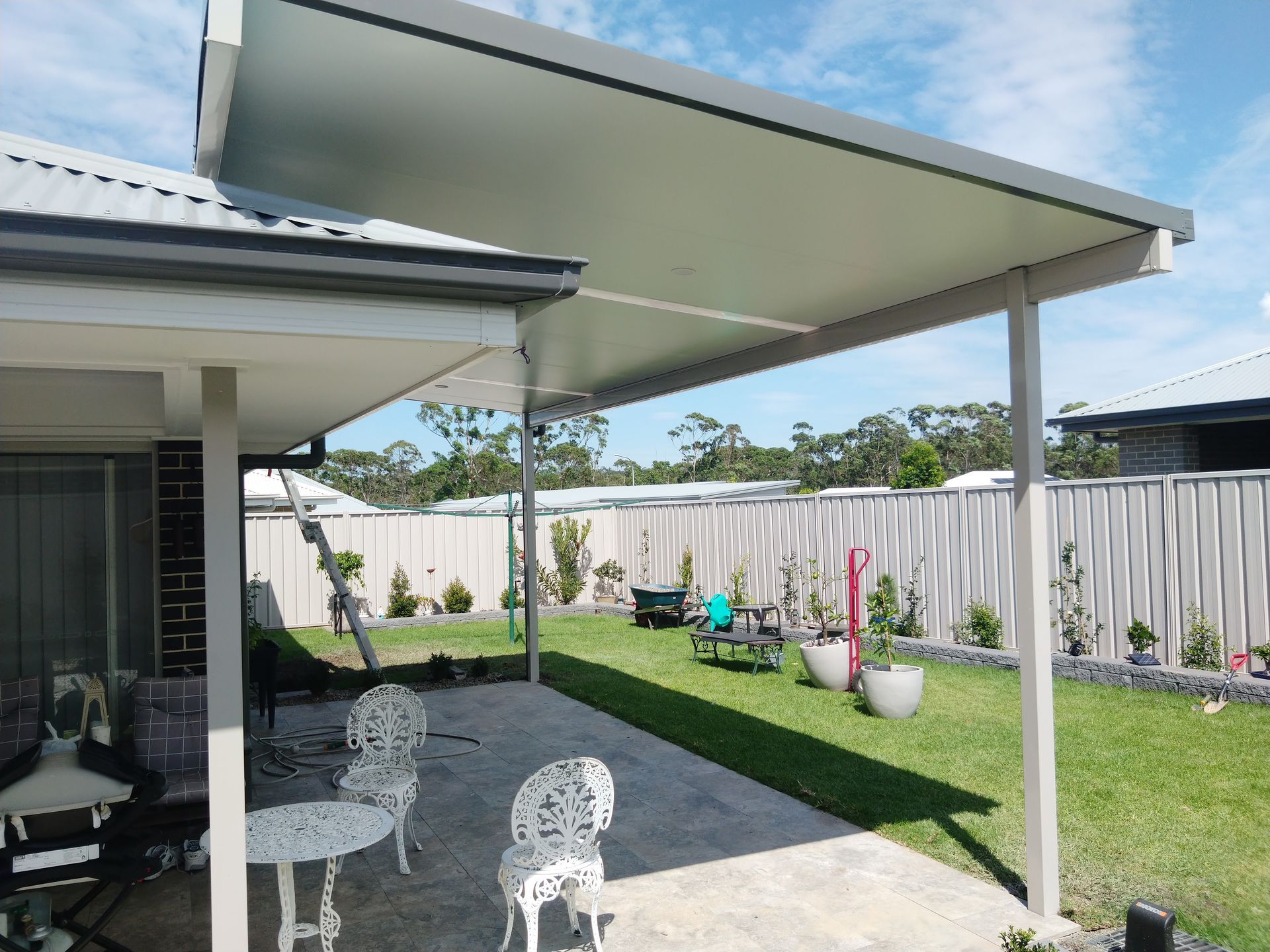 A white patio cover is being installed on the side of a brick house.