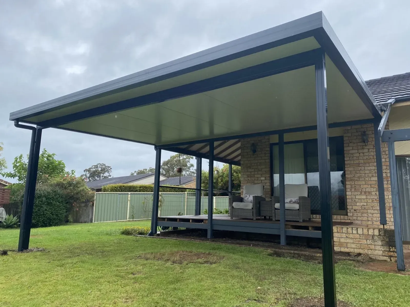 A white patio cover is being installed on the side of a brick house.