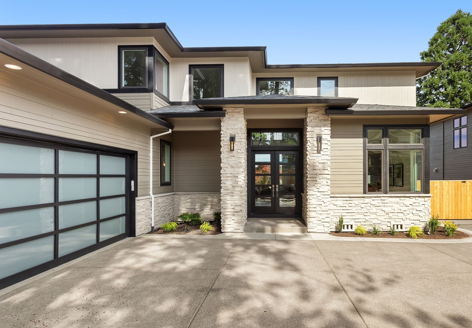 A modern two-story home with a tan exterior, stone accents, a multi-panel frosted garage door, and a glass-paneled entry.