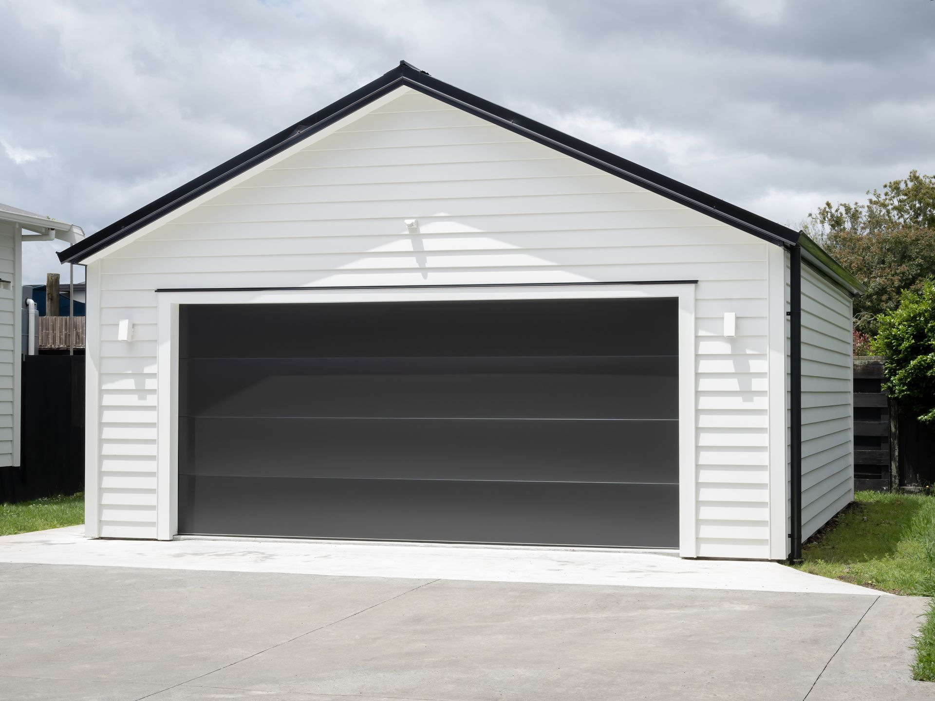 A white, single-story garage with horizontal siding, a dark gray sectional door, and a black roof trim, set on concrete.