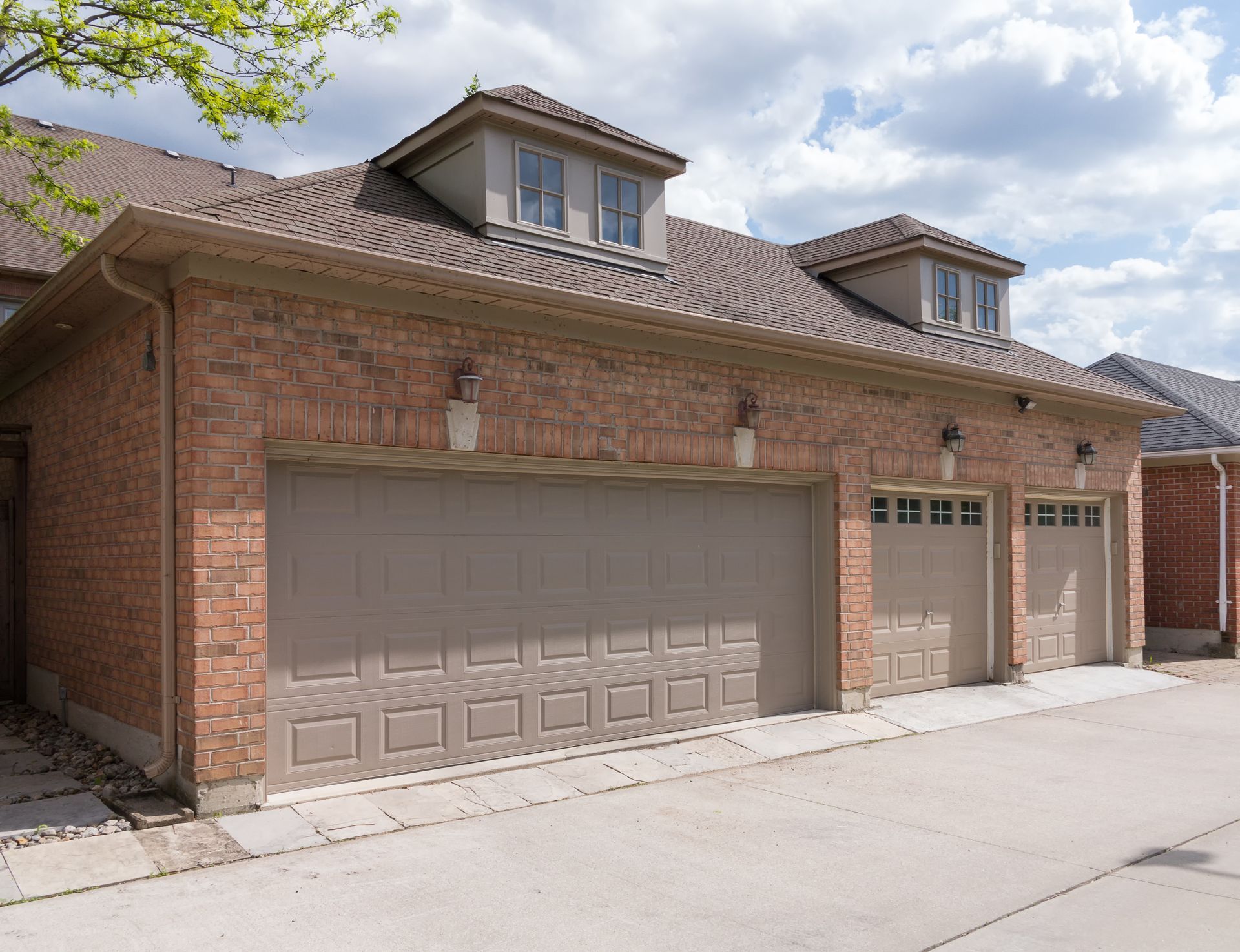 Brick suburban house with two-car garage and driveway under a partly cloudy sky