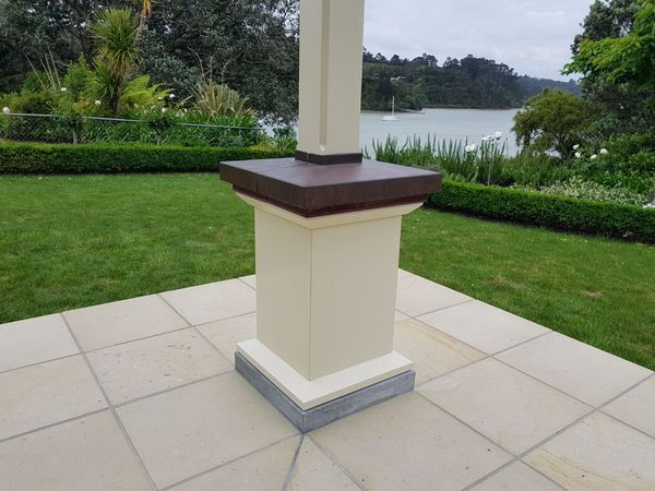 A white column with a brown top sits on a tiled patio in front of a lush green field.