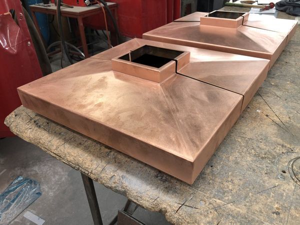 Three square copper pieces are sitting on a table.