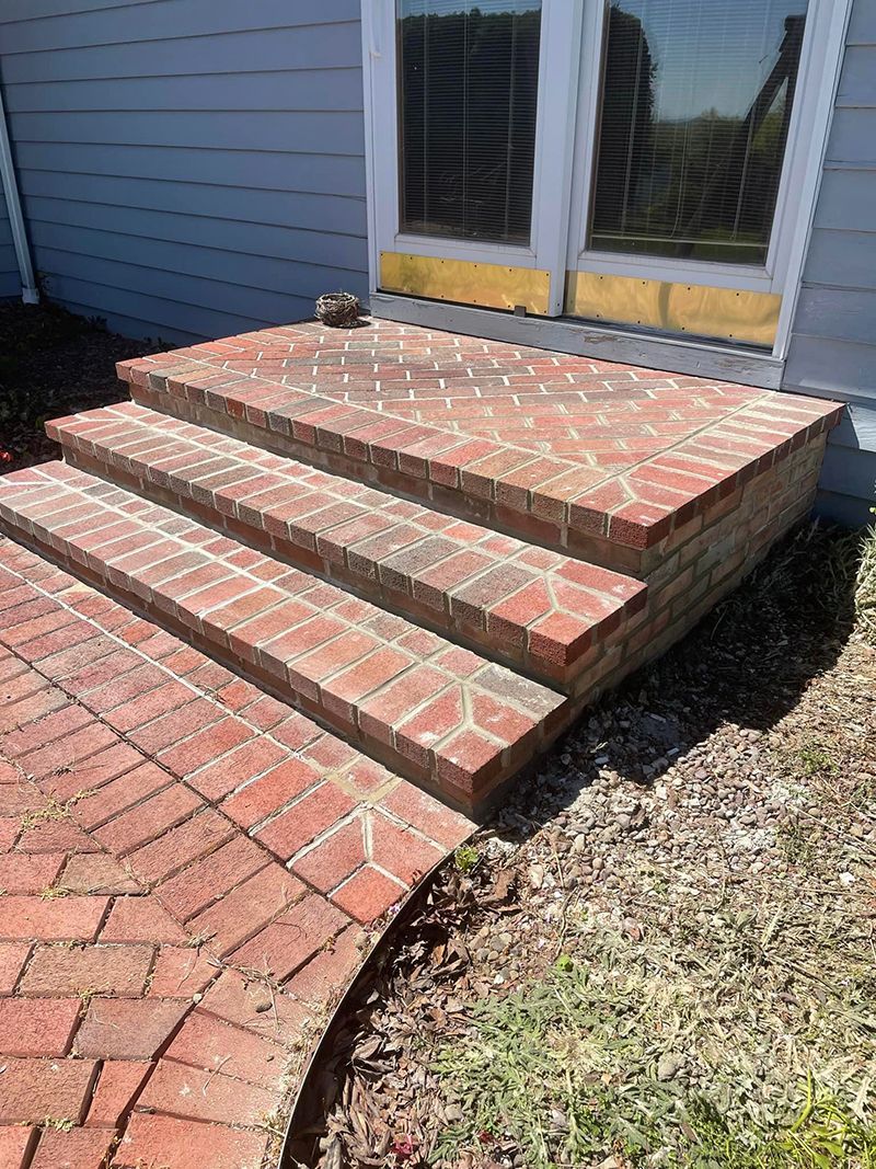 Brick steps leading up to a door. Red brick patio in front.