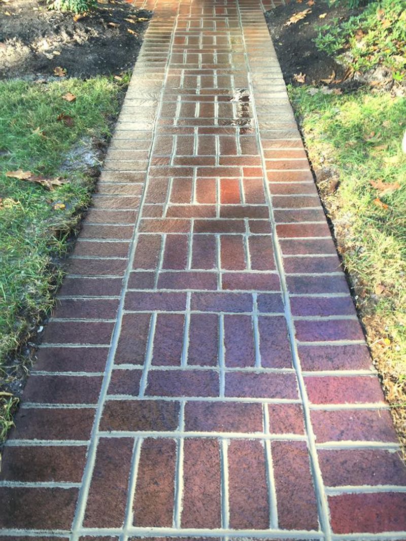 Brick walkway in a herringbone and running bond pattern, bordered by grass and soil.