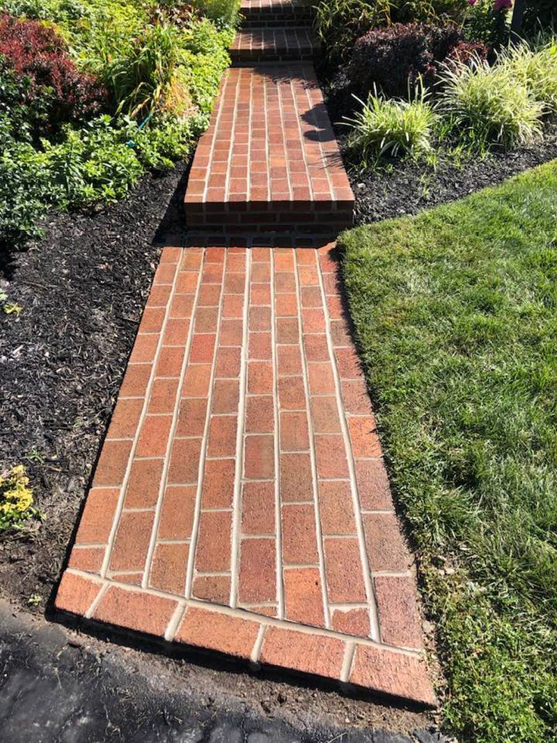Brick walkway leading up steps, surrounded by green grass and mulch with plants.