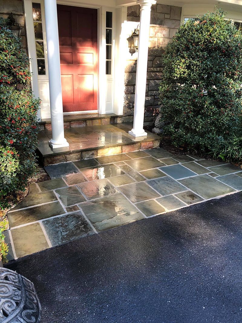 Stone walkway leading to a house with a red door, white columns, and green bushes.