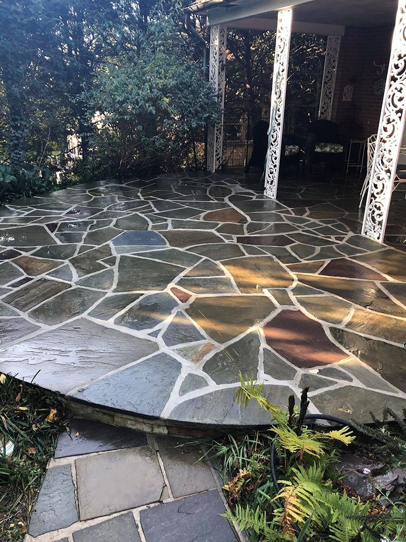 Flagstone patio with an arched entrance, surrounded by lush greenery and ornate pillars.