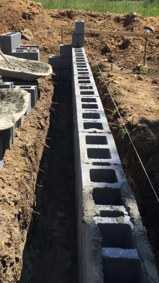 Concrete blocks stacked in a trench, forming a wall foundation. Soil visible around the structure.