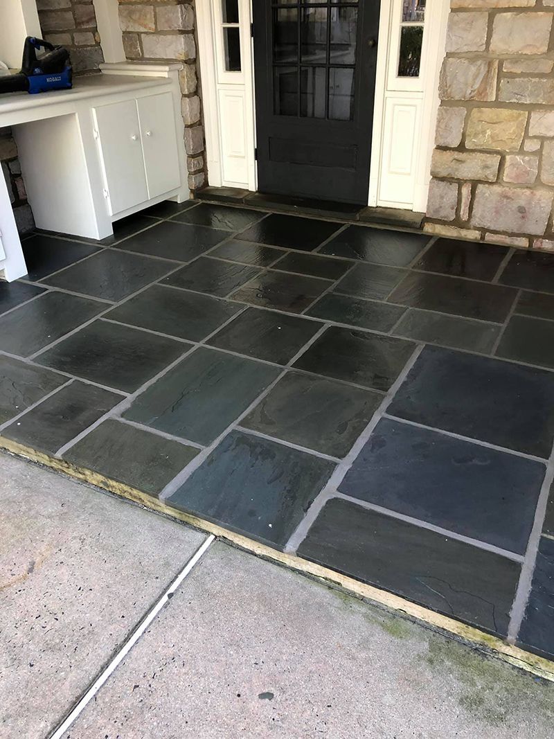 Dark blue flagstone patio with gray grout, in front of a gray door and white cabinets.