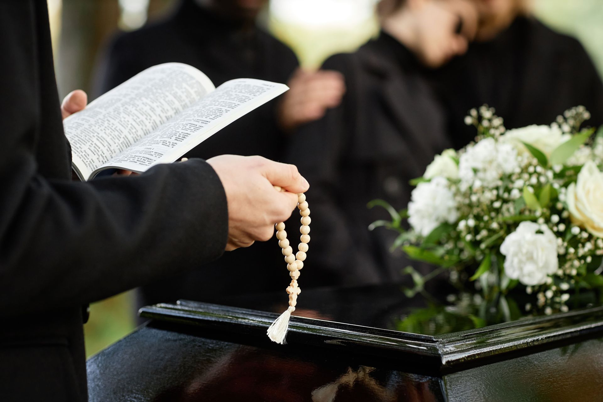 person in black praying at funeral and holding Bible with rosary