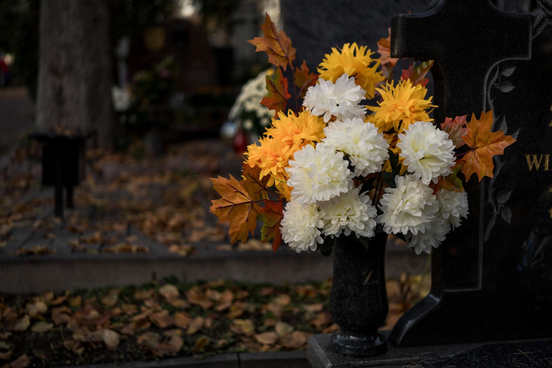 Autumn flower bouquet on a grave covered with fallen dry leaves in a cemetery
