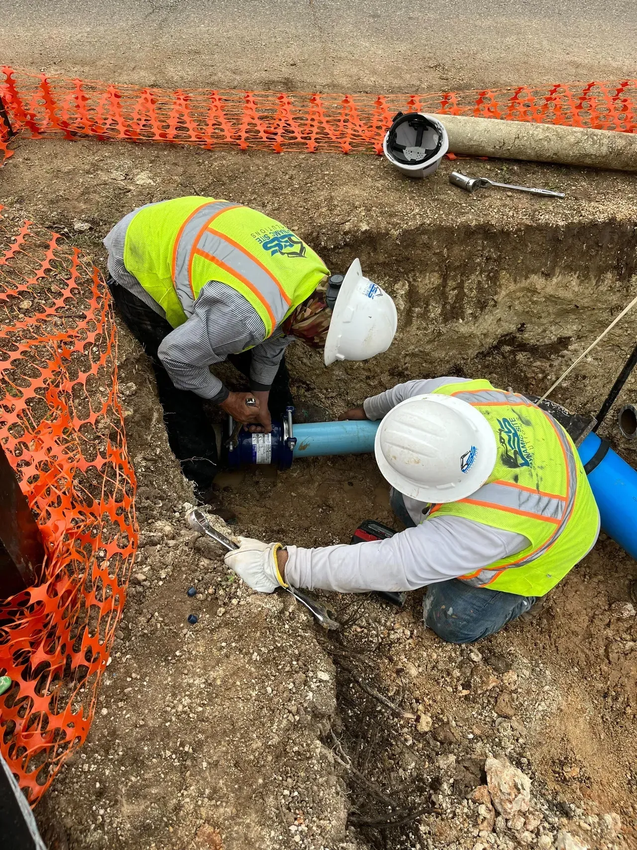 Two construction workers are working on a pipe in the dirt.
