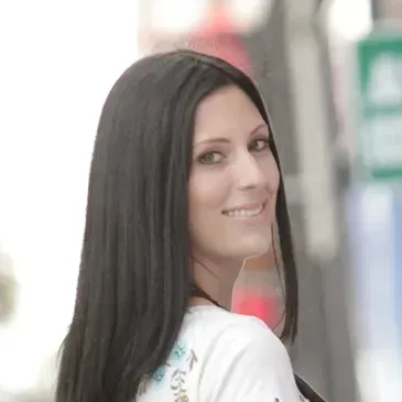 A woman with long black hair is smiling and looking over her shoulder.