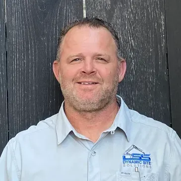 A man with a beard is wearing a blue shirt and smiling.