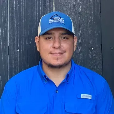 A man wearing a blue shirt and a blue hat is standing in front of a wooden wall.