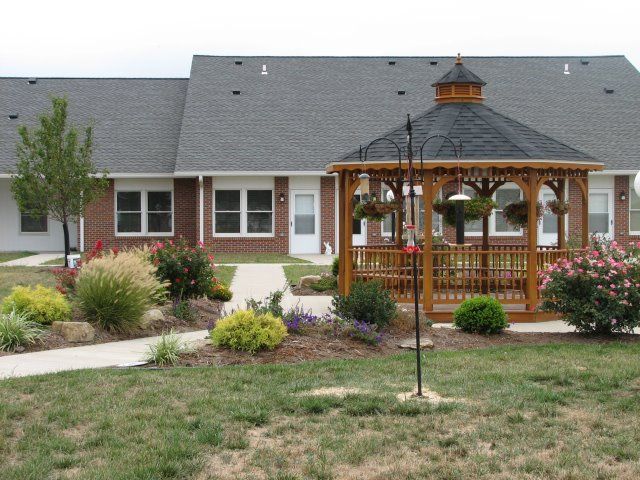 Gazebo in a landscaped garden with a brick building in the background.