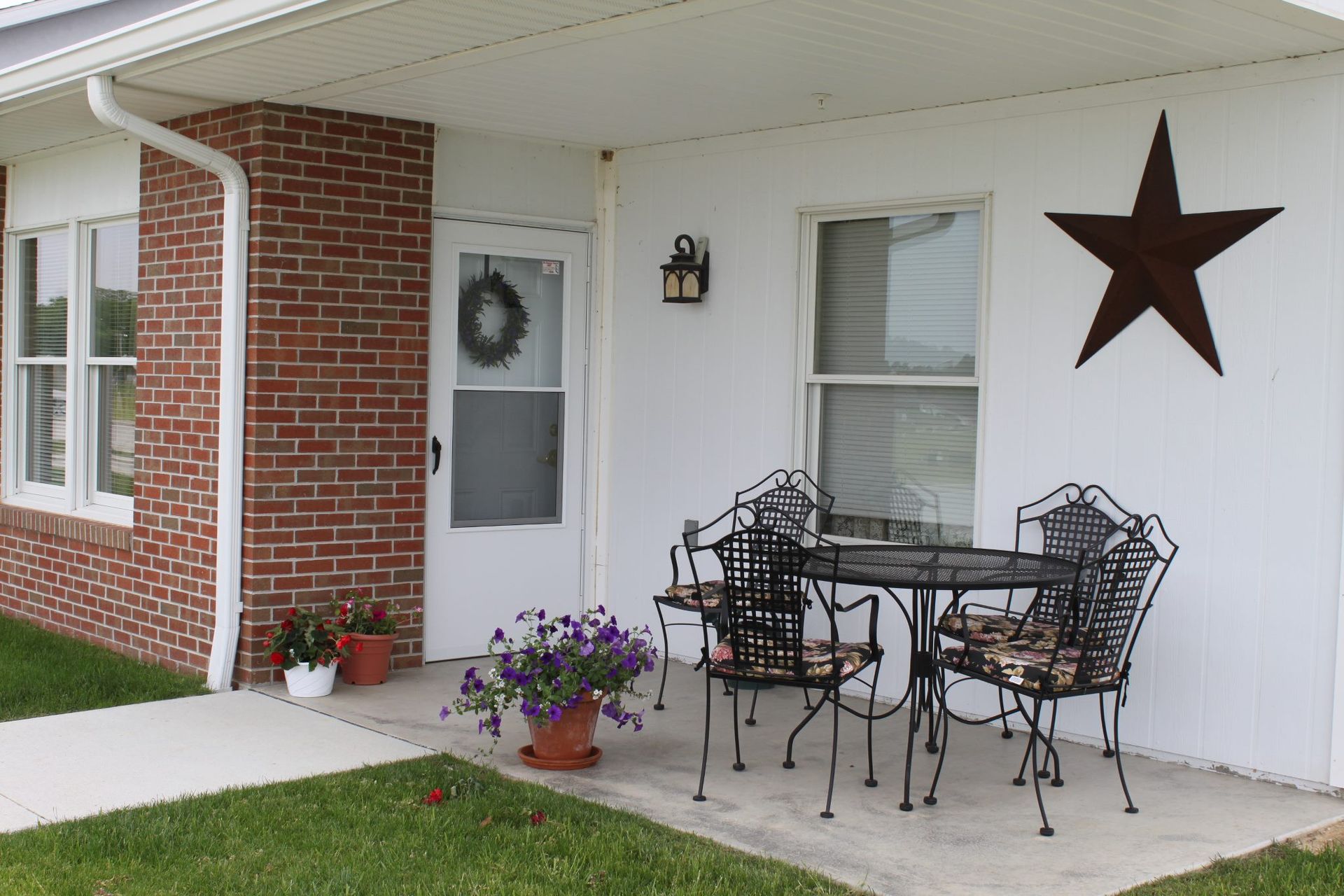 Porch of a brick building with a metal table and chairs, a star, and potted plants.