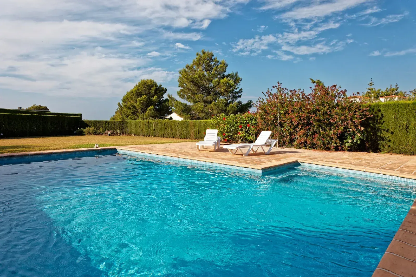 Backyard swimming pool with blue water, white lounge chairs, and a sunny sky