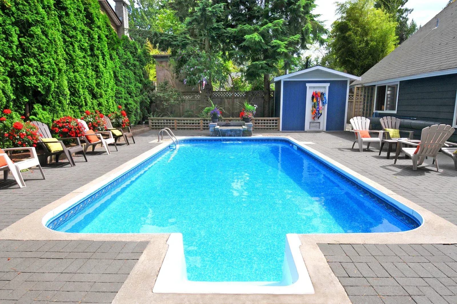 Backyard swimming pool with lounge chairs, potted flowers, and a blue shed on a sunny day