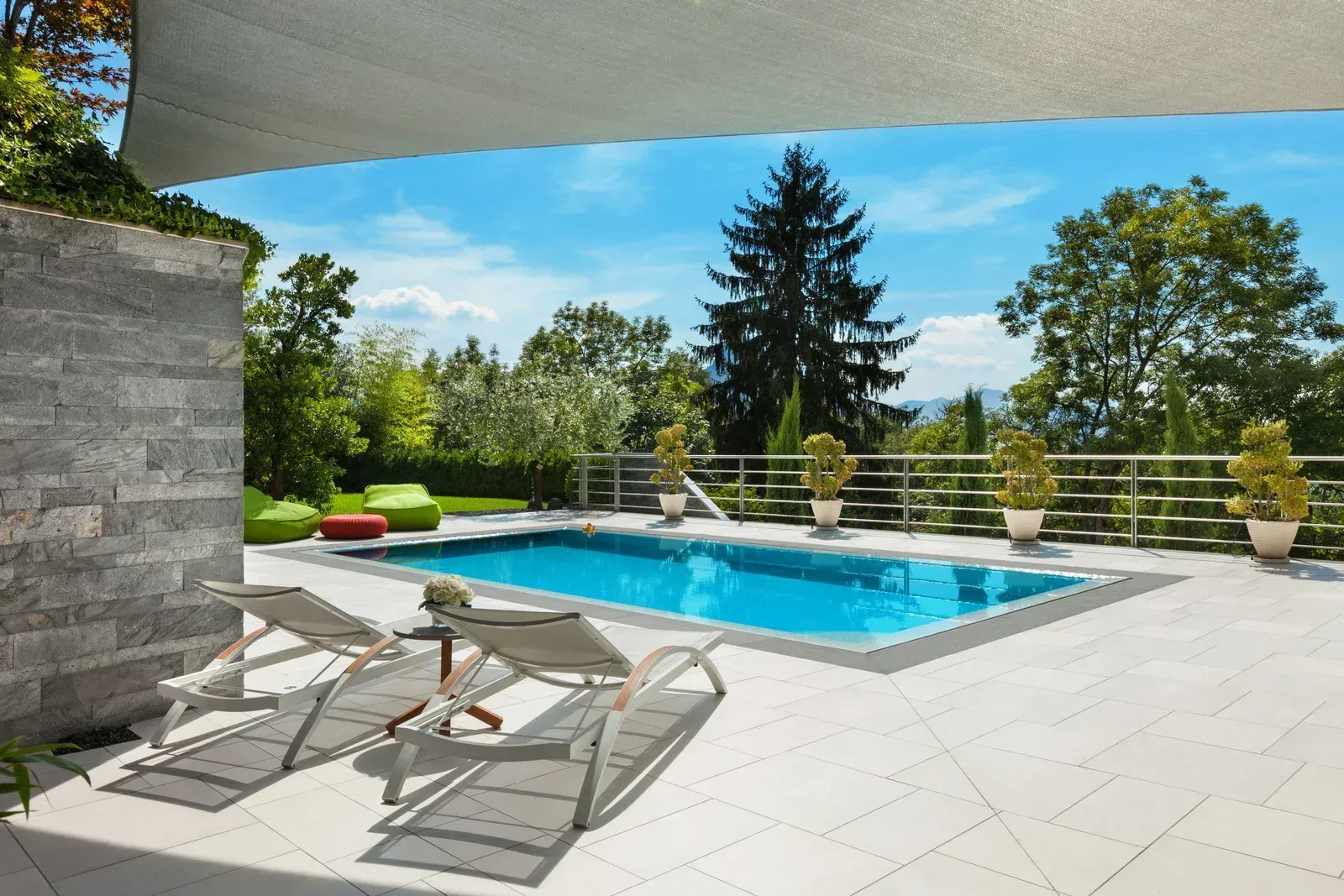 Modern backyard pool with lounge chairs, tiled patio, and trees under a shaded canopy