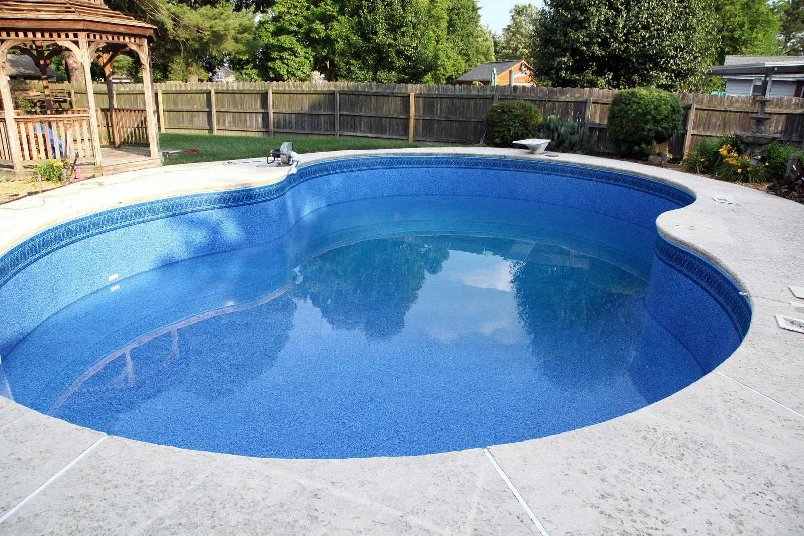 Backyard swimming pool with blue water, white stone deck, and gazebo in the background