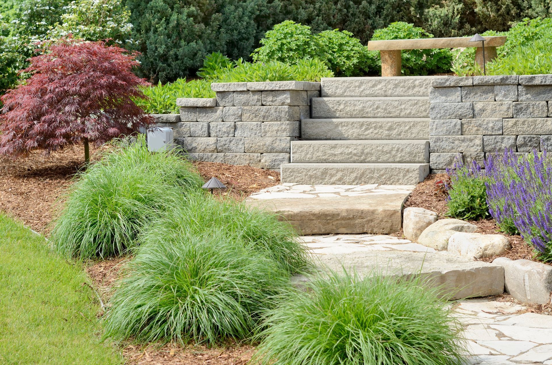 Brick planter box with yellow lilies and pink flowers in a paved courtyard.