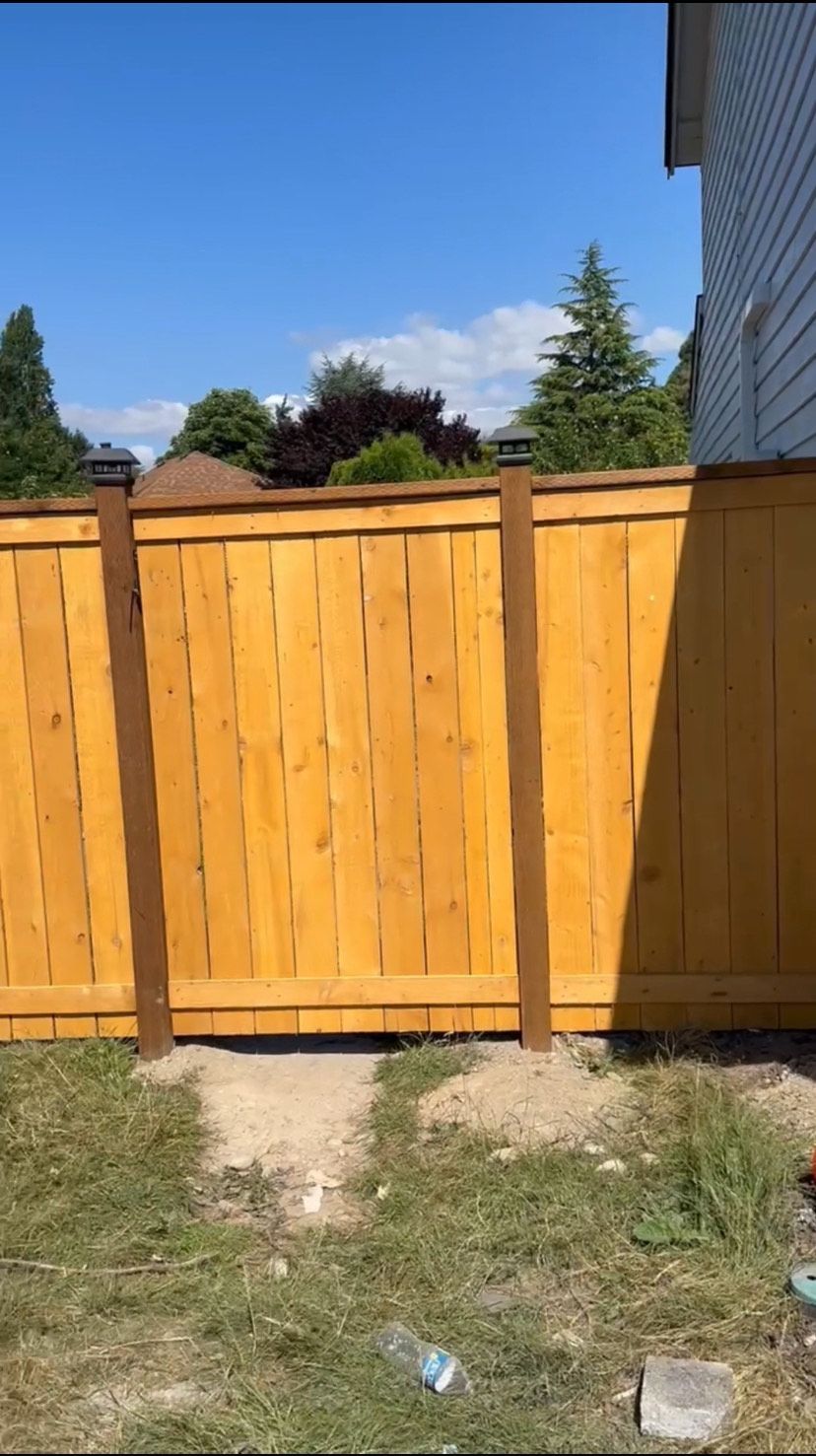 Man hammering on a fence, wearing work clothes, set against a cloudy sky.