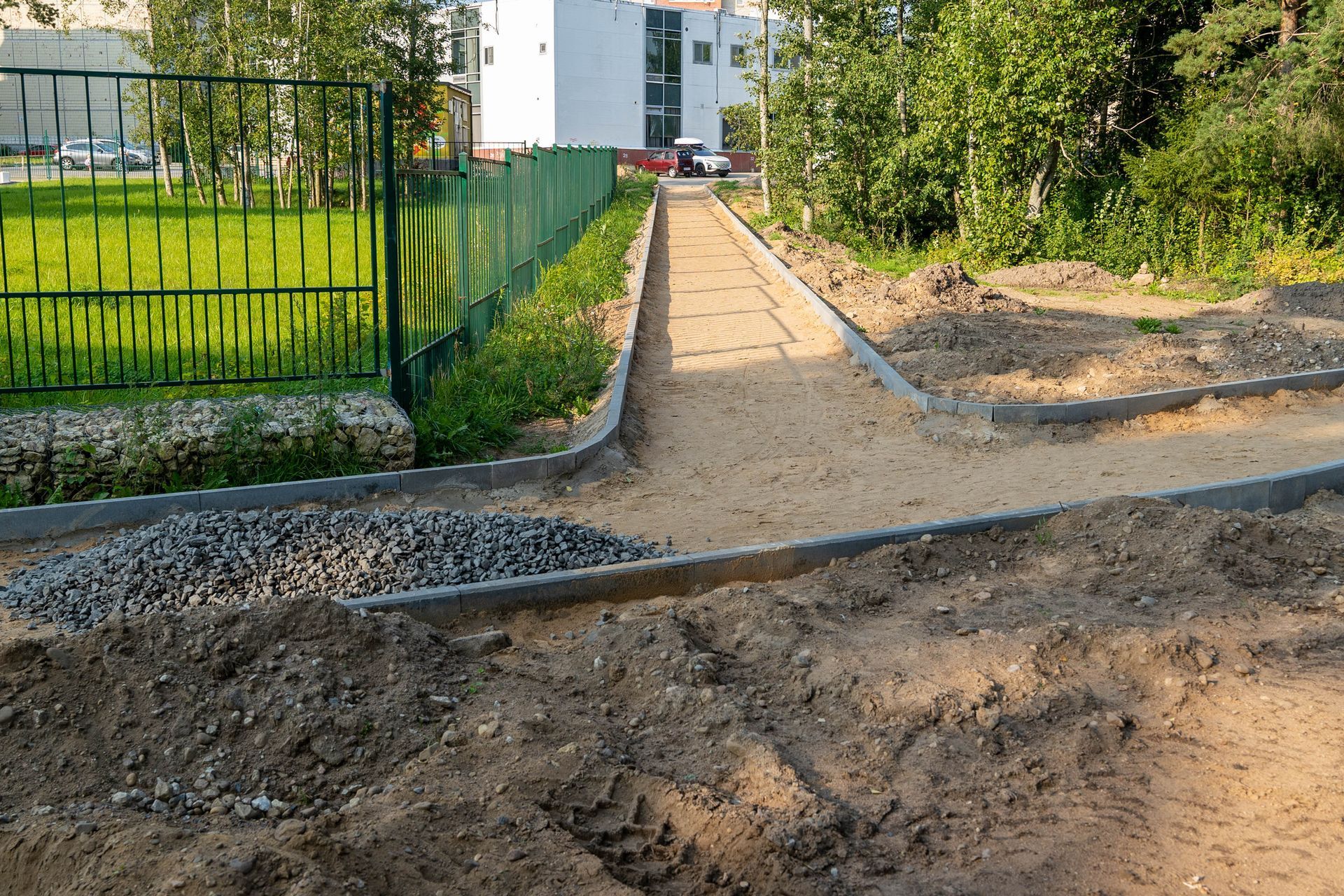 Pathway under construction with gravel and dirt in a green space.