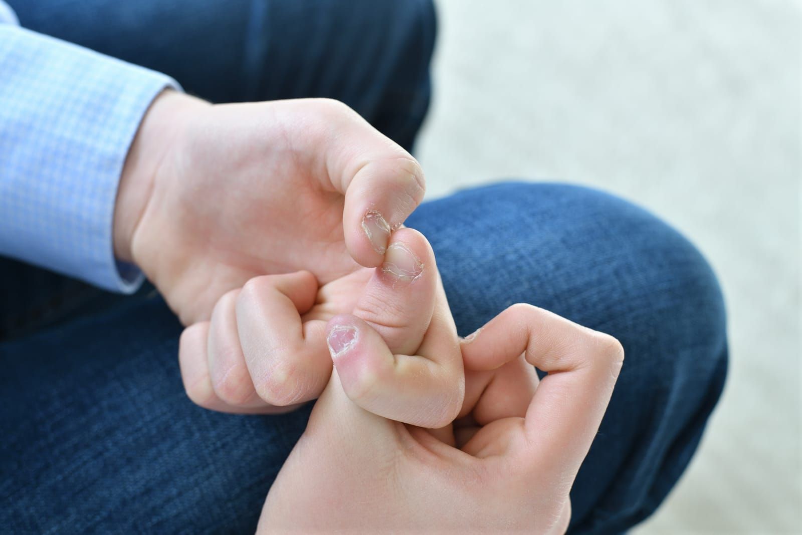A close-up of hands pulling on cuticles and skin around the fingernails, indicating the habit of nail biting or picking.