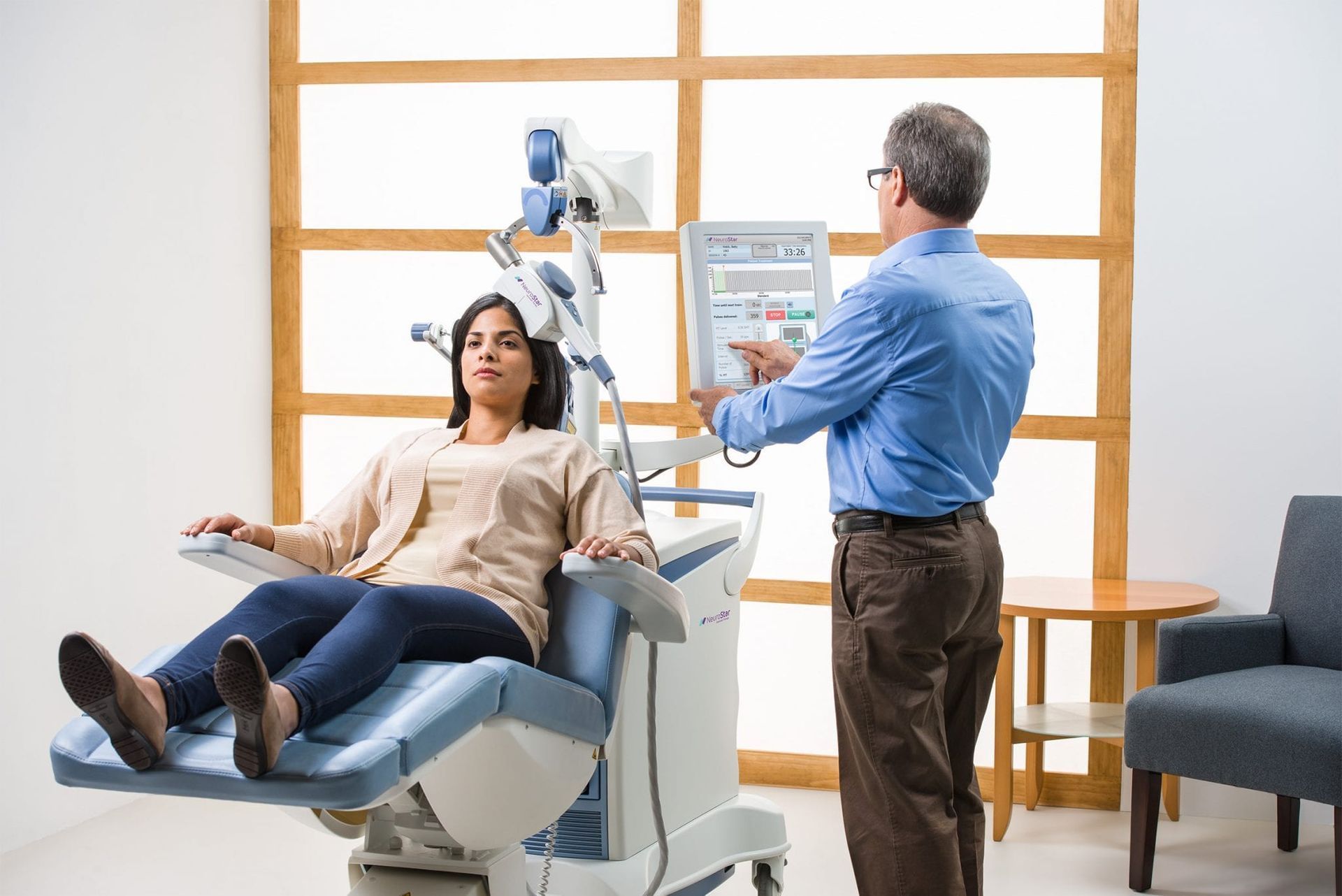 Woman in medical chair undergoing procedure, with technician adjusting equipment.