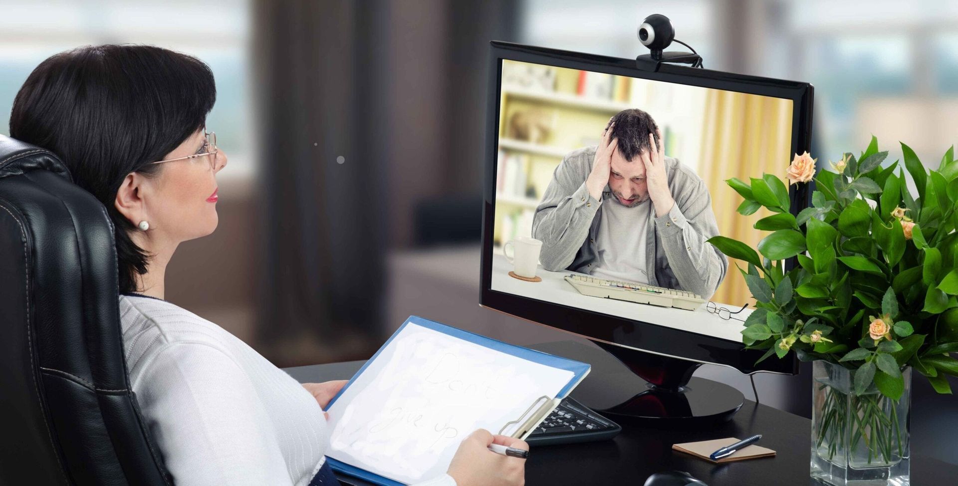 A woman in a chair consults with a person on a computer screen. The person on the screen looks stressed.