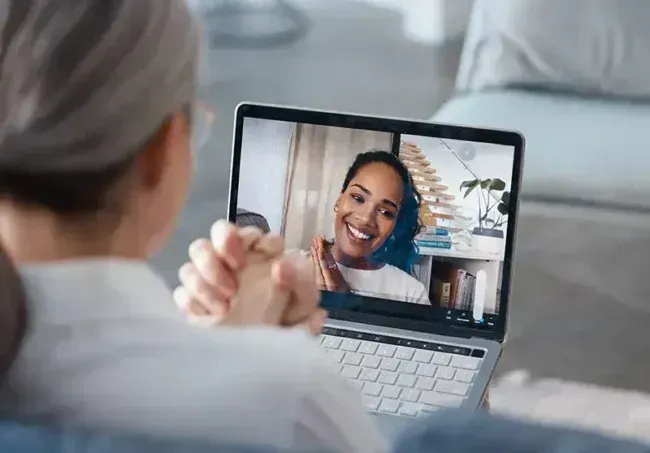 Woman on laptop video call smiles at person on screen.