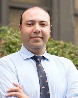 Man with crossed arms wearing a blue shirt and patterned tie.