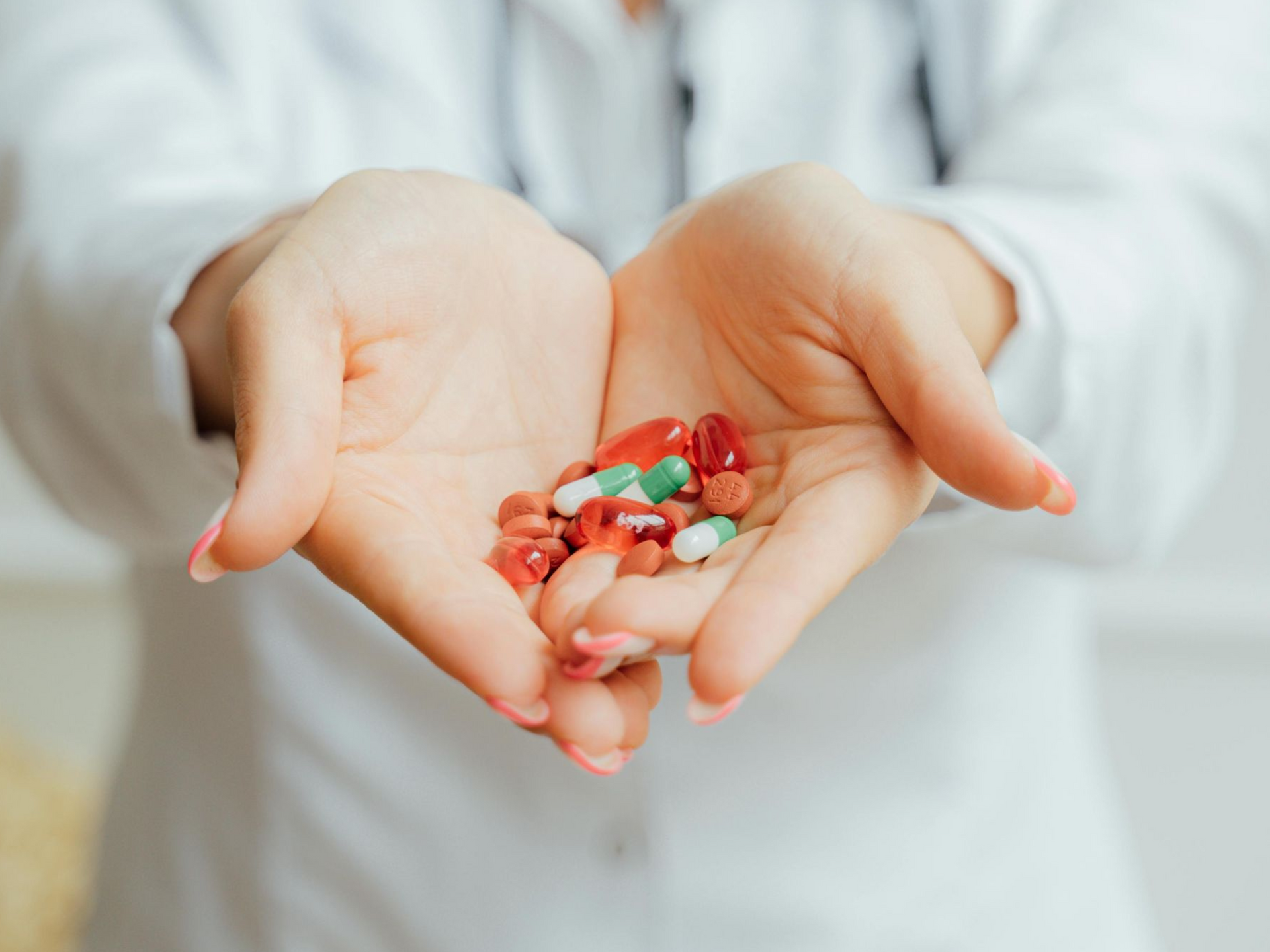 Hands of a person in a white coat holding a variety of colorful pills.