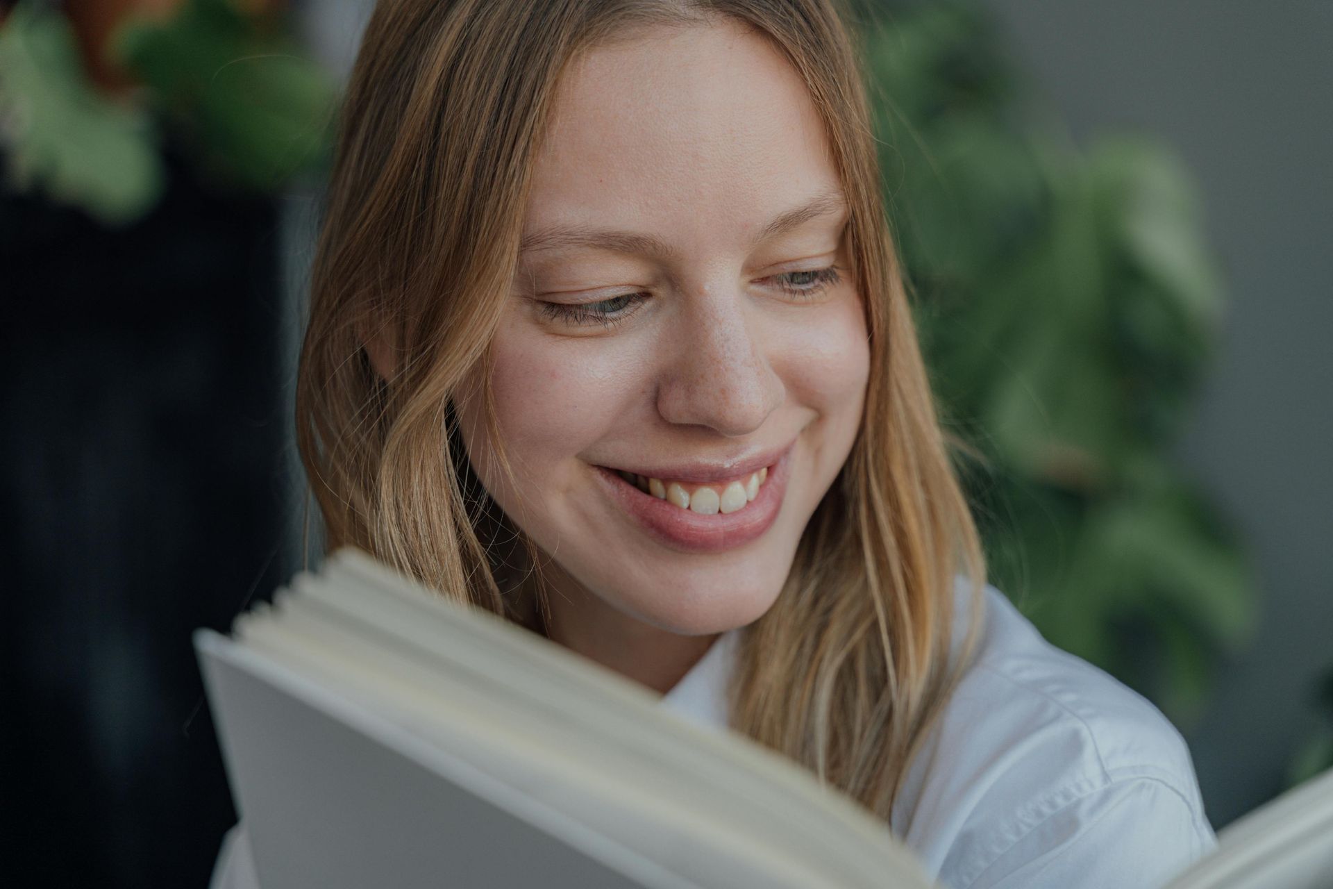Woman with light brown hair smiles while reading a book.
