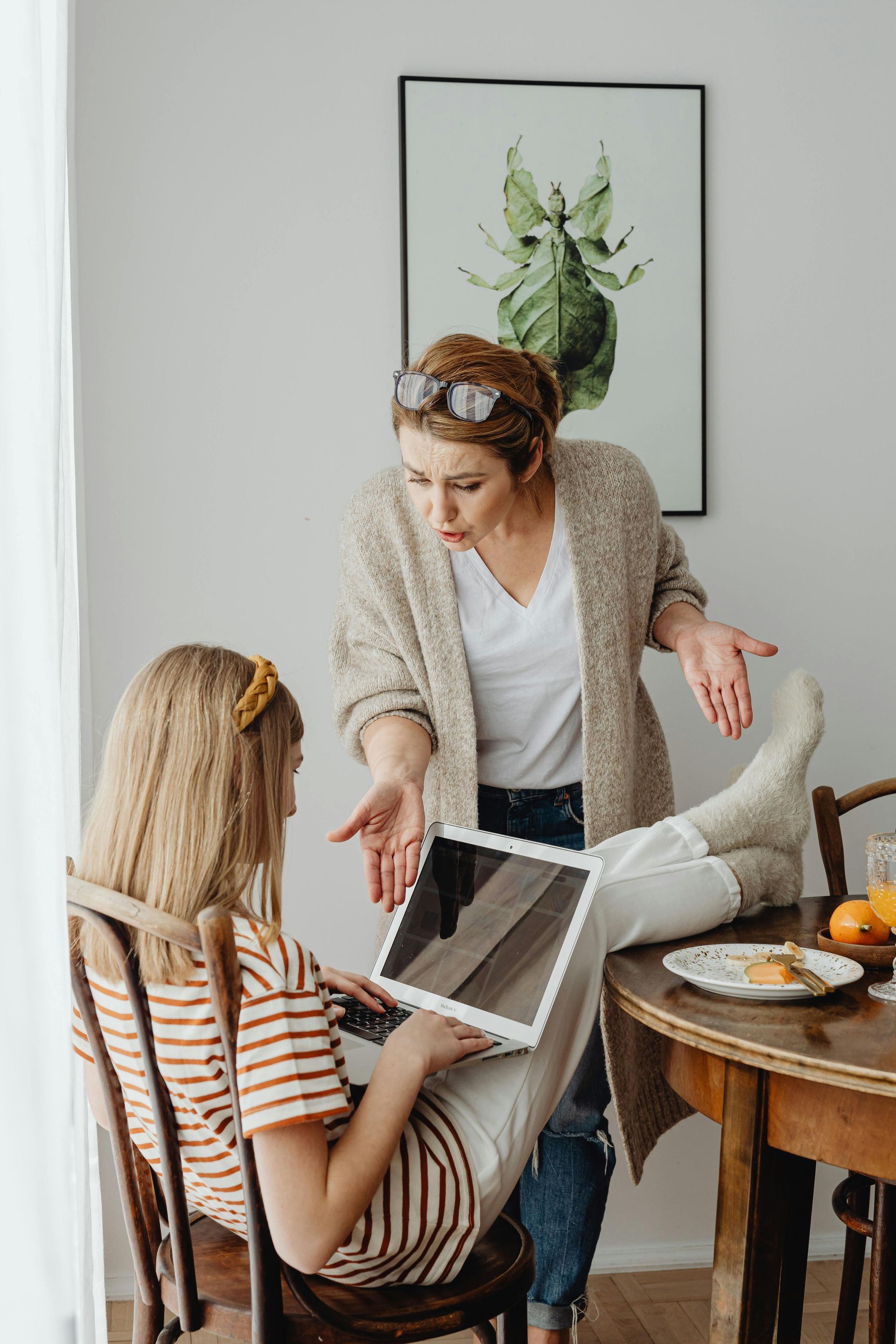 A person stands beside a seated person using a laptop, gesturing as if in a tense or serious discussion.