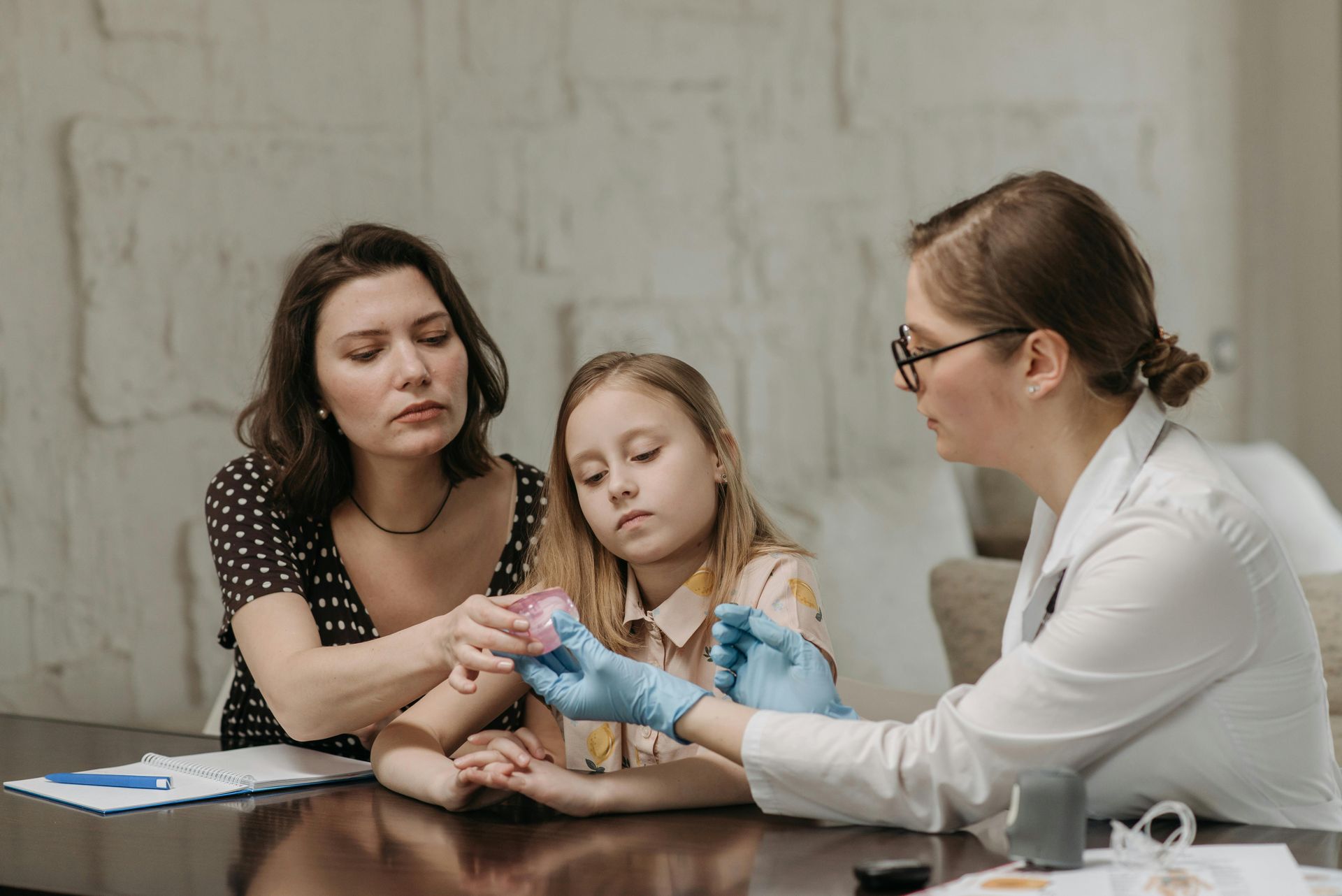 A doctor showing a mother and child a medical device at a table, indoors.