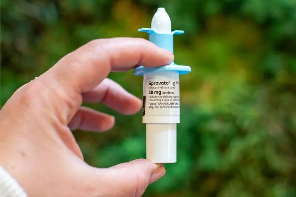Hand holding a blue and white nasal spray against a blurry green background.