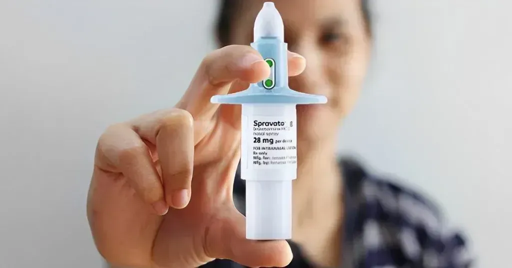 Person holding a nasal spray bottle, in front of a neutral background.