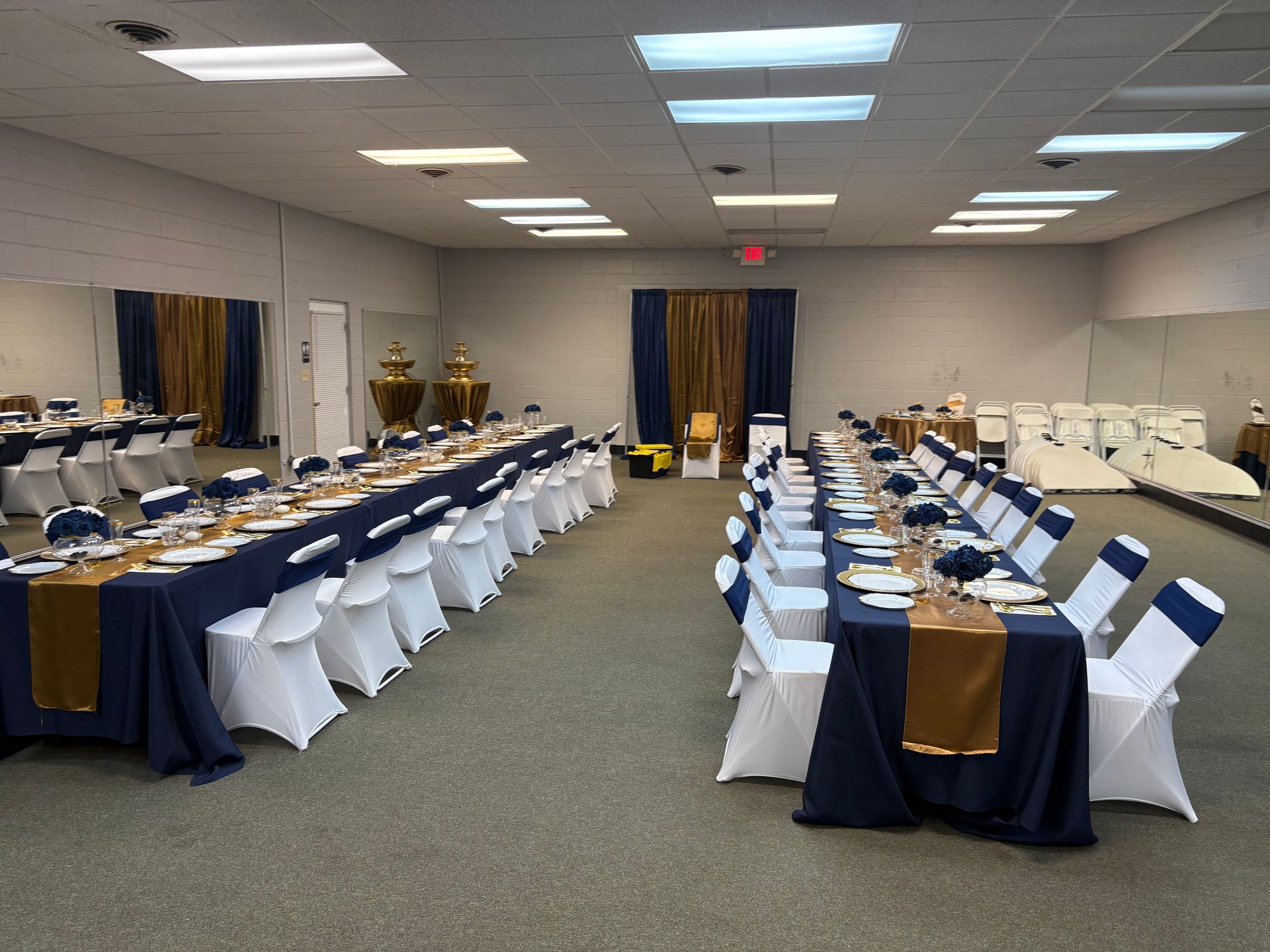 Event hall with long tables set with navy and gold decor, white chairs, and an ornate backdrop.