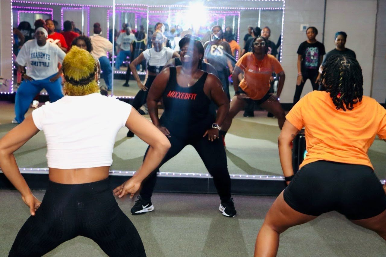 A group of people are dancing in front of a mirror and one of them is wearing an orange shirt with the number 23 on it