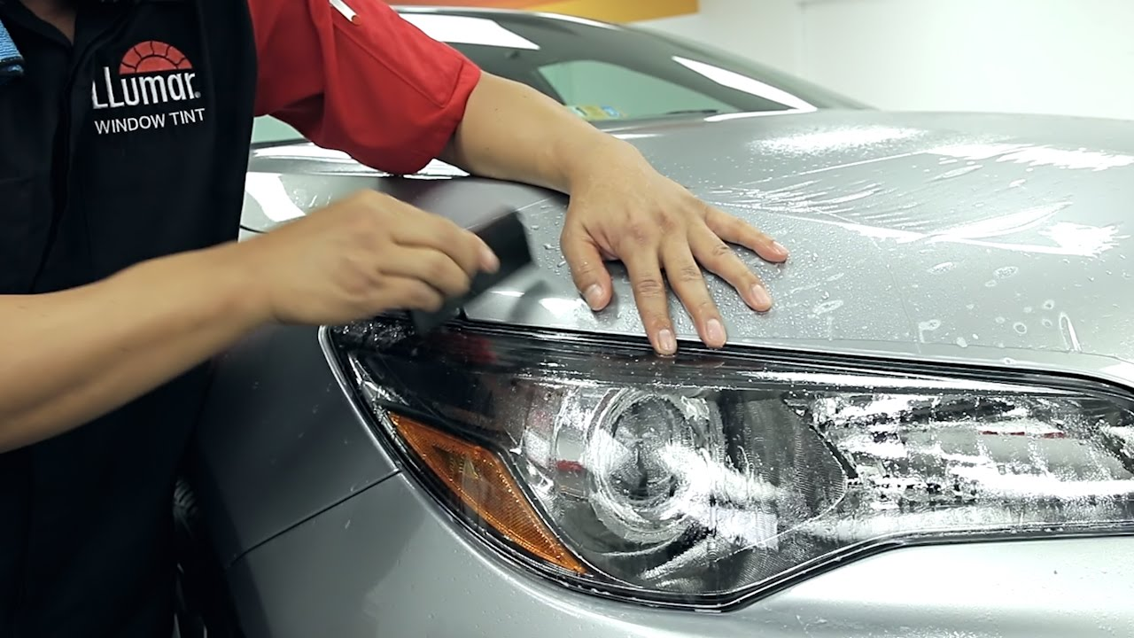 A man is applying a protective film to the headlight of a car.  - Fullerton, CA - Ace Auto Tint, Inc.