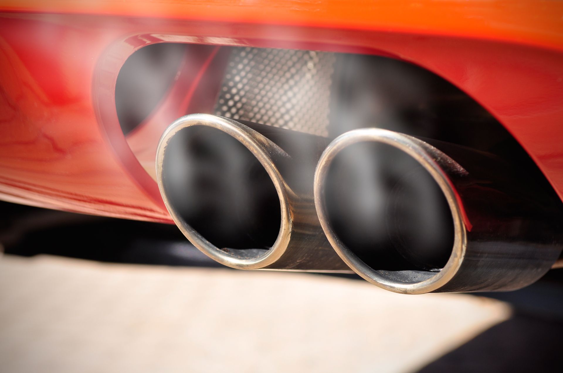 Close-up of a red car's exhaust pipes releasing white smoke.