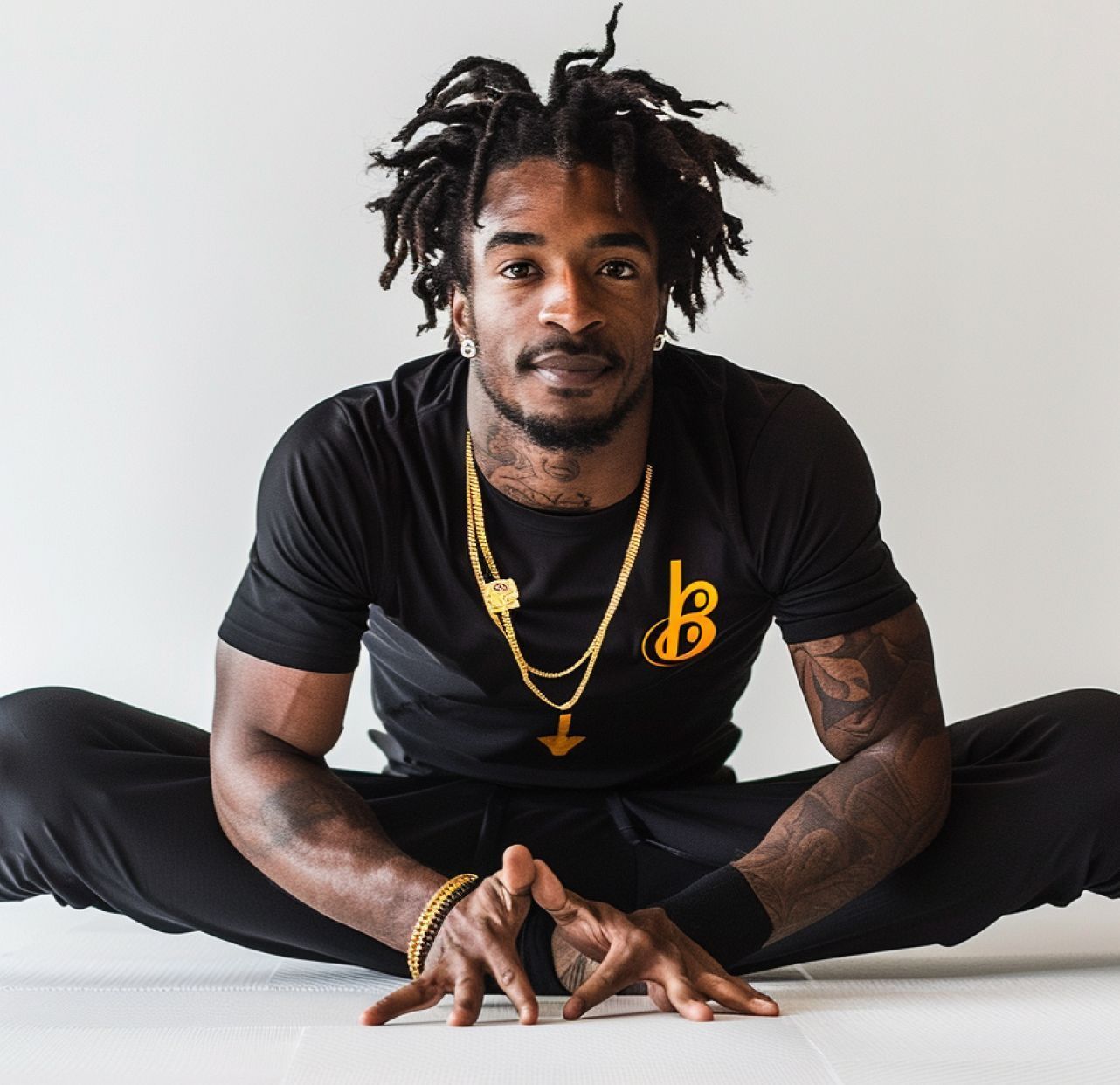 A man is sitting on the floor wearing a black shirt with the letter b on it