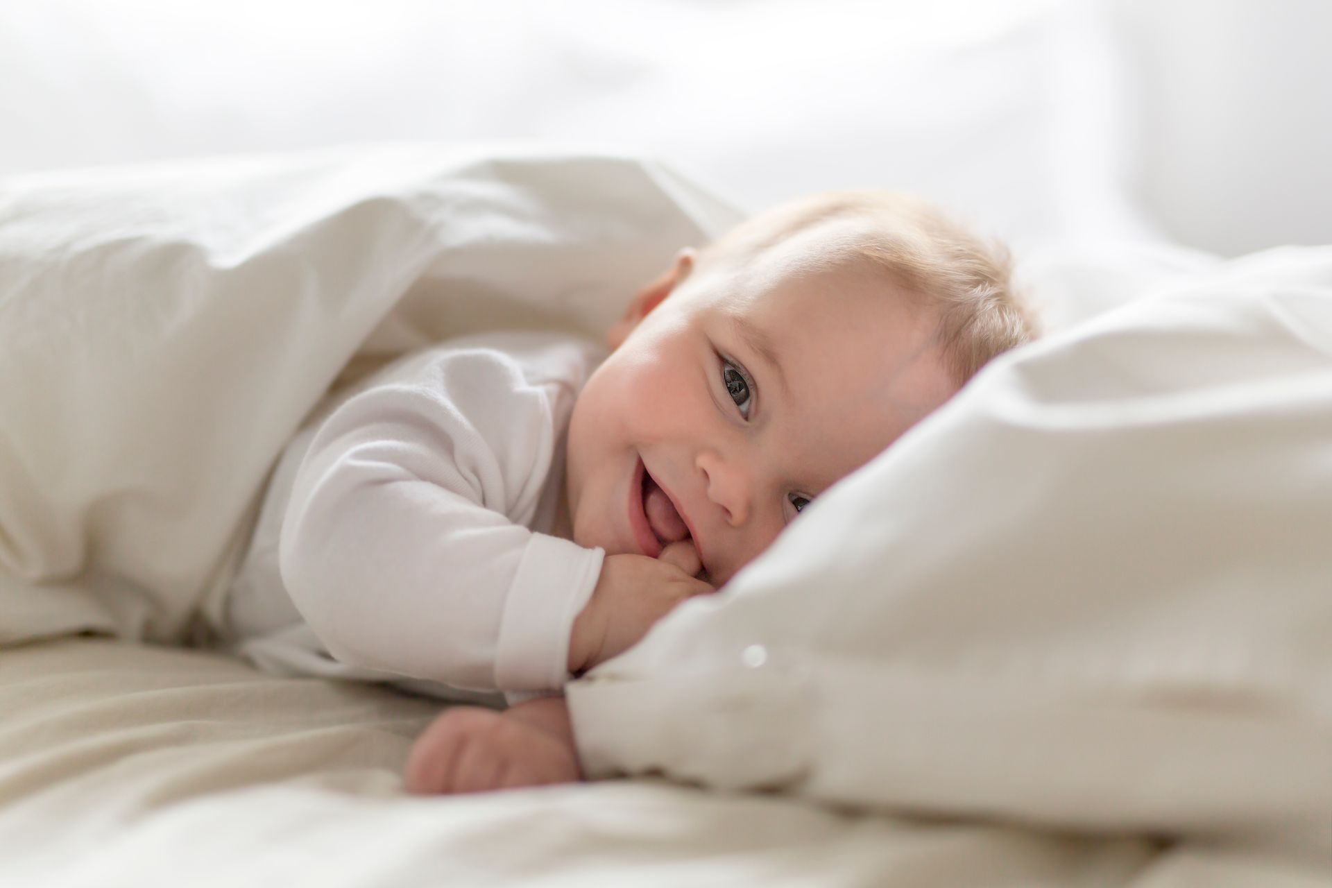 A baby is laying on a bed under a blanket and smiling.