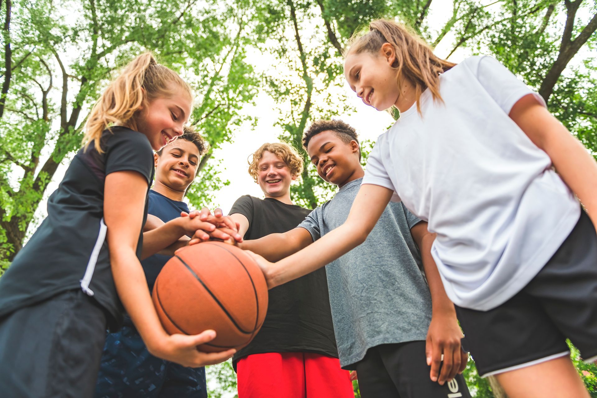 A group of young people are putting their hands on a basketball.