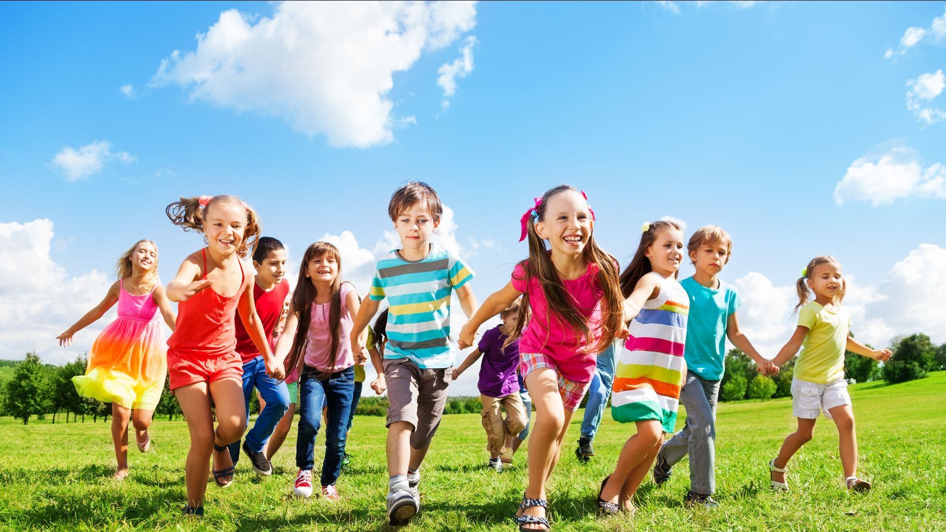 A group of children are running in a field holding hands.