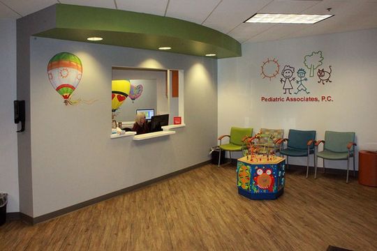 A waiting room with chairs , a table and a hot air balloon on the wall.