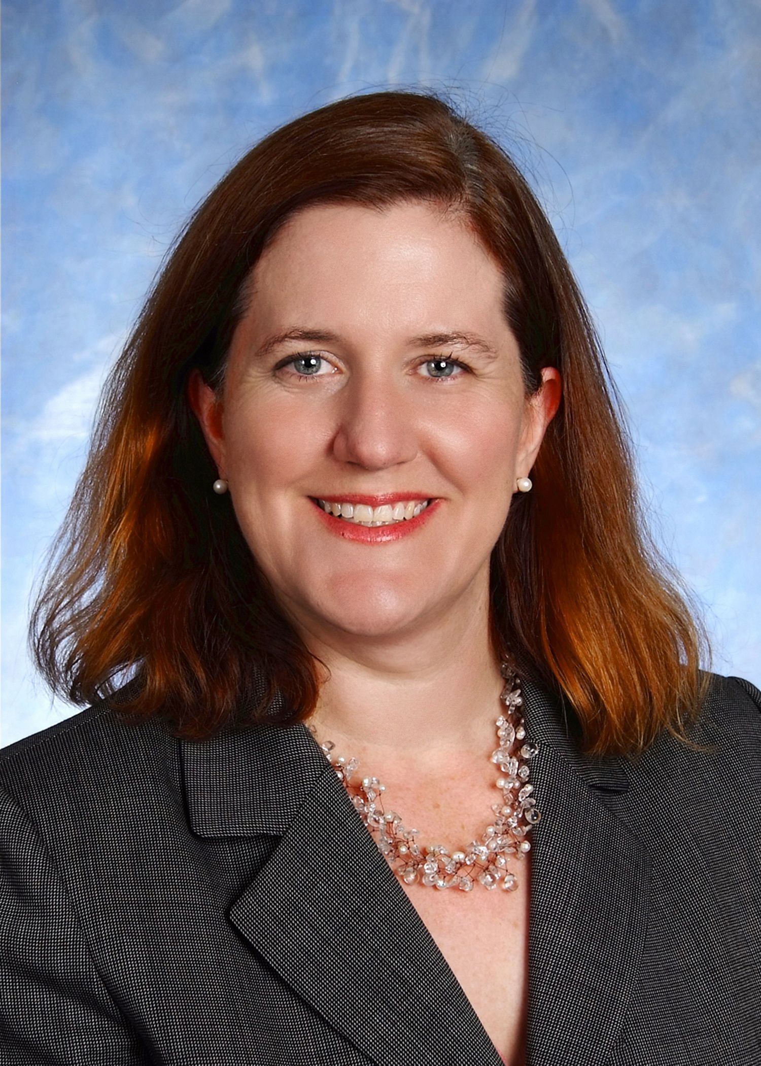 A woman with red hair is wearing a black and white jacket and a necklace.